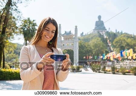 "Young female tourist reviewing smartphone photographs in front of Tian Tan Buddha, Po Lin Monastery, Lantau Island, Hong Kong, China" View Large Photo Image Stock Image - "Young female tourist reviewing smartphone photographs in front of Tian Tan Buddha, Po Lin Monastery, Lantau Island, Hong Kong, China". Fotosearch