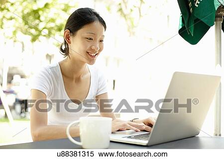 Stock Photography - "Young female tourist typing on laptop at sidewalk cafe, The Bund, Shanghai, China". Fotosearch