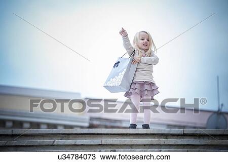 Stock Image - "Young girl pointing from stairway carrying shopping bag, Cagliari, Sardinia, Italy". Fotosearch