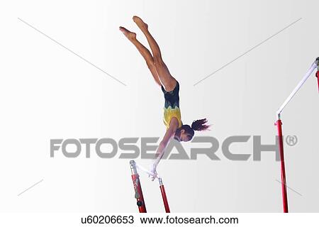 Stock Image - Young gymnast performing on uneven bars. Fotosearch