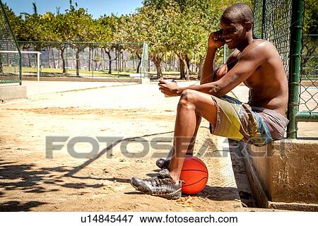 Stock Photo - Young male basketball player chatting on smartphone and drinking water. Fotosearch