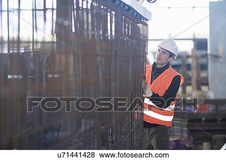 Stock Photo - Young male factory worker choosing wire mesh in concrete reinforcement factory. Fotosearch