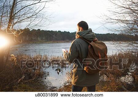 Stock Photo - Young male hiker at lakeside reading map. Fotosearch