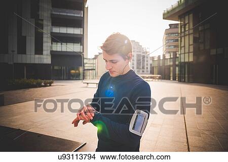 Young male runner checking wrist watch in city square View Large Photo Image Picture - Young male runner checking wrist watch in city square. Fotosearch