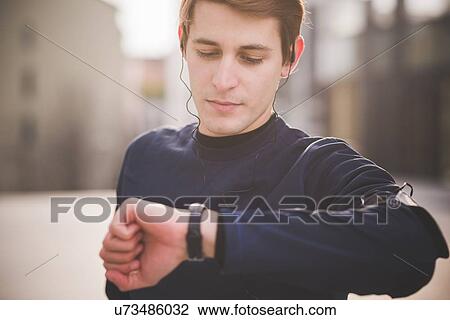 Young male runner checking wristwatch in city square View Large Photo Image Stock Image - Young male runner checking wristwatch in city square. Fotosearch