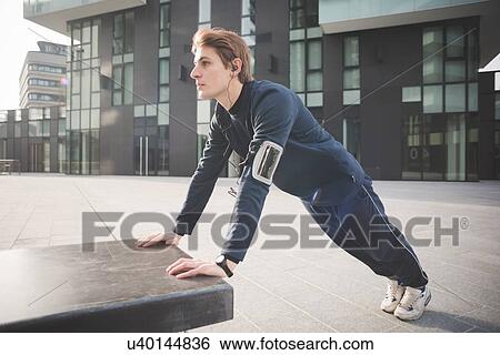 Young male runner doing push ups on bench in city square View Large Photo Image Stock Photograph - Young male runner doing push ups on bench in city square. Fotosearch