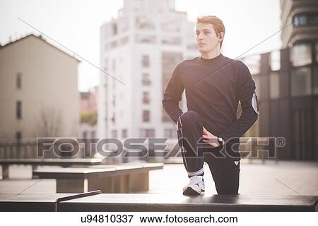 Stock Photo - Young male runner doing warm up in city square. Fotosearch