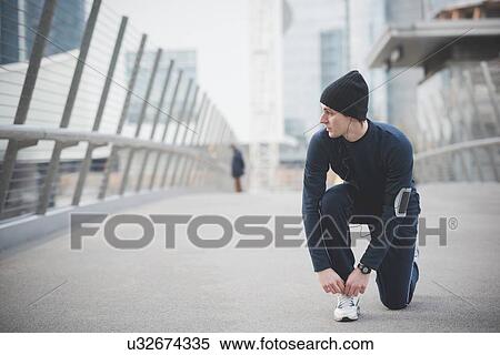 Young male runner fastening trainer lace on city footbridge View Large Photo Image Stock Photography - Young male runner fastening trainer lace on city footbridge. Fotosearch