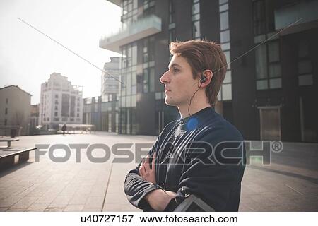 Stock Photo - Young male runner listening to earphones in city square. Fotosearch