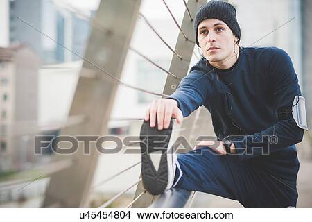 Picture - Young male runner touching toes on city footbridge. Fotosearch