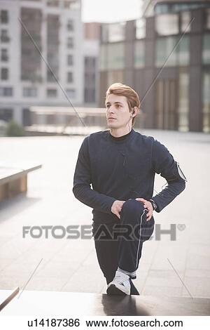 Stock Photograph - Young male runner warming up in city square. Fotosearch