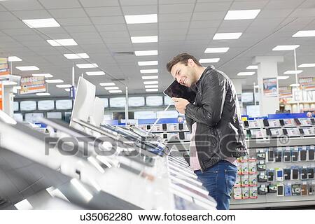 Young male shopper holding up chosen digital tablet in electronics store View Large Photo Image Stock Image - Young male shopper holding up chosen digital tablet in electronics store. Fotosearch