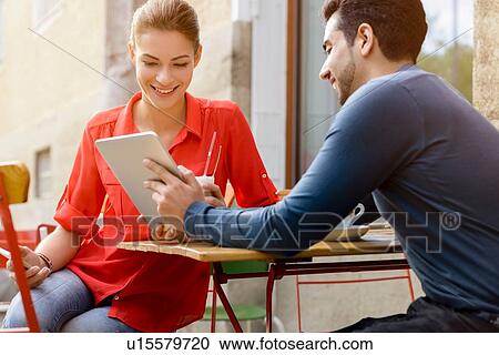 "Young man and woman sitting outside cafe, looking at digital tablet" View Large Photo Image Stock Image - "Young man and woman sitting outside cafe, looking at digital tablet". Fotosearch
