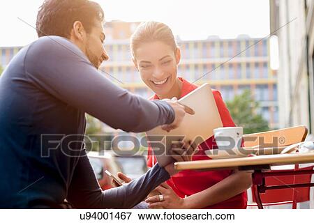 "Young man and woman sitting outside cafe, looking at digital tablet" View Large Photo Image Stock Photo - "Young man and woman sitting outside cafe, looking at digital tablet". Fotosearch