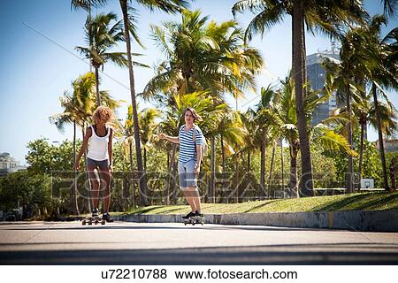 Young man and woman skateboarding along road View Large Photo Image Stock Photo - Young man and woman skateboarding along road. Fotosearch