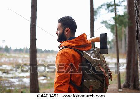 Stock Image - Young man carrying axe looking out from forest. Fotosearch