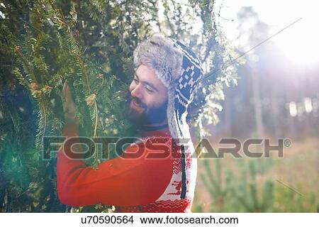 Picture - Young man carrying Christmas tree on shoulders in woods. Fotosearch