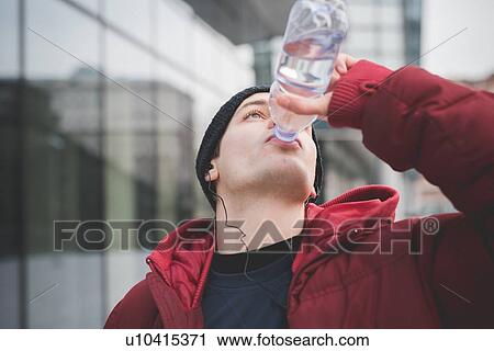 Stock Image - Young man drinking water outside city office. Fotosearch