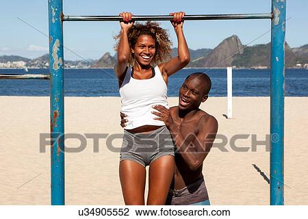 Stock Image - Young man helping woman do chin ups. Fotosearch