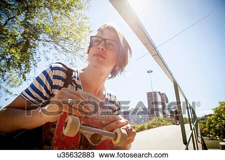 "Young man holding skateboard, low angle view" View Large Photo Image Stock Image - "Young man holding skateboard, low angle view". Fotosearch
