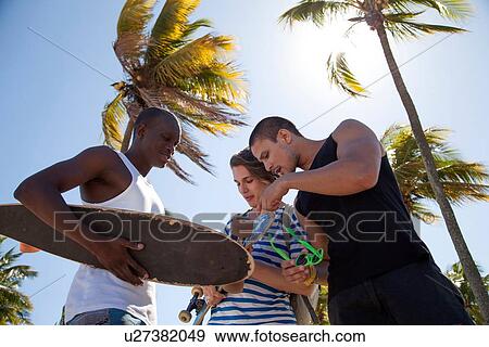 "Young man holding skateboard with friends, low angle" View Large Photo Image Stock Photo - "Young man holding skateboard with friends, low angle". Fotosearch