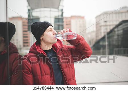 Young man leaning against office building drinking water View Large Photo Image Picture - Young man leaning against office building drinking water. Fotosearch