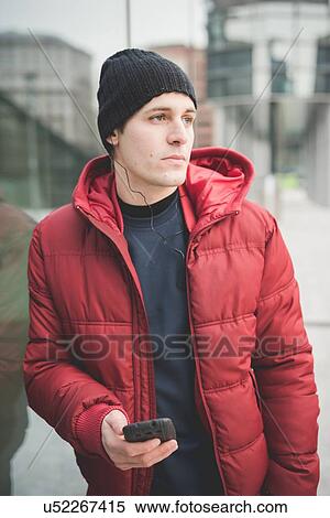 Stock Photography - Young man leaning against office building reading smartphone texts. Fotosearch