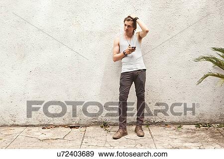 Young man leaning texting on smartphone on street View Large Photo Image Stock Photo - Young man leaning texting on smartphone on street. Fotosearch