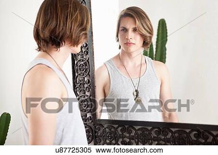 Stock Photography - Young man looking at mirror image in hotel lobby. Fotosearch