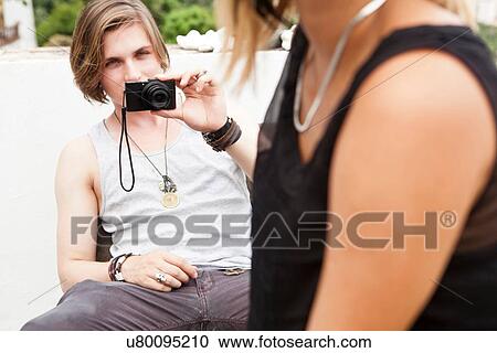 Stock Image - Young man photographing girlfriend on hotel roof garden. Fotosearch