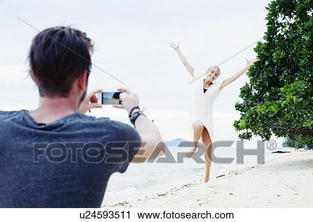 "Young man photographing girlfriend jumping on beach, Kradan, Thailand" View Large Photo Image Stock Image - "Young man photographing girlfriend jumping on beach, Kradan, Thailand". Fotosearch