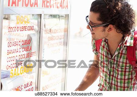 Picture - "Young man reading food stall menu, Copacabana, Rio De Janeiro, Brazil". Fotosearch