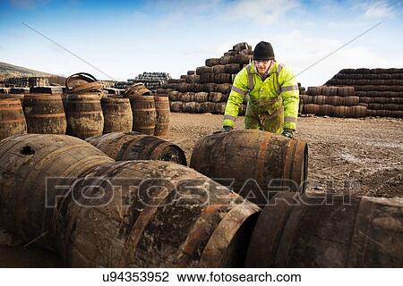 Stock Image - Young man rolling whisky cask at cooperage. Fotosearch
