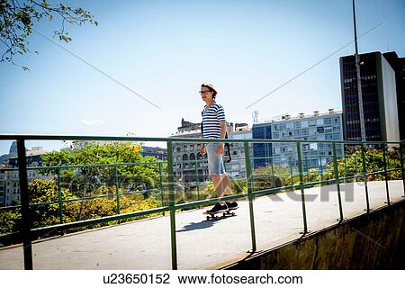Stock Image - Young man skateboarding along walkway. Fotosearch