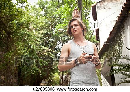 Young man strolling on street texting on smartphone View Large Photo Image Stock Photograph - Young man strolling on street texting on smartphone. Fotosearch