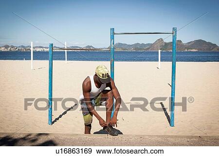 Stock Photo - Young man tying shoelace on beach. Fotosearch