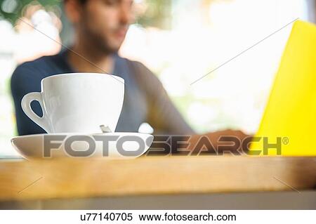 Stock Photography - "Young man using laptop in cafe, low angle view". Fotosearch