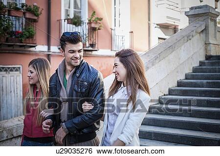 Stock Photograph - "Young man with female friends strolling along street, Cagliari, Sardinia, Italy". Fotosearch