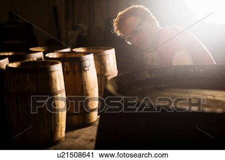 Stock Image - Young man working in cooperage with whisky casks. Fotosearch