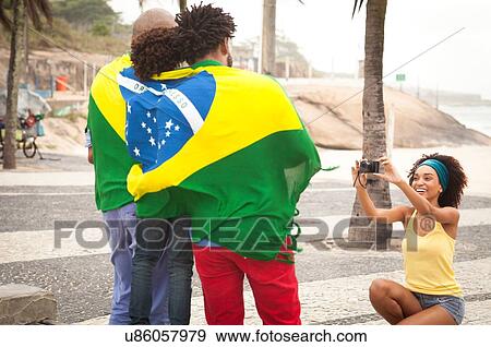 Stock Photo - "Young mother photographing family wrapped in Brazilian flag on Ipanema beach, Rio De Janeiro, Brazil". Fotosearch