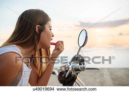 "Young woman applying lipstick in motorcycle wing mirror, Manila, Philippines" View Large Photo Image Picture - "Young woman applying lipstick in motorcycle wing mirror, Manila, Philippines". Fotosearch