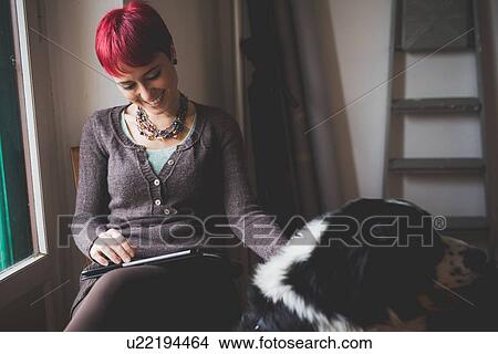 "Young woman at home using digital tablet, stroking dog" View Large Photo Image Picture - "Young woman at home using digital tablet, stroking dog". Fotosearch
