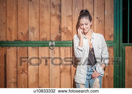 Young woman by stable on cell phone View Large Photo Image Stock Image - Young woman by stable on cell phone. Fotosearch