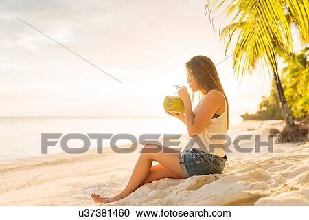 Stock Image - "Young woman drinking fresh coconut milk on Anda beach, Bohol Province, Philippines". Fotosearch