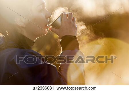 Young woman drinking hot drink in sunlight View Large Photo Image Stock Image - Young woman drinking hot drink in sunlight. Fotosearch