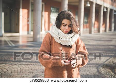 Young woman examining headphone cable on street View Large Photo Image Stock Photograph - Young woman examining headphone cable on street. Fotosearch