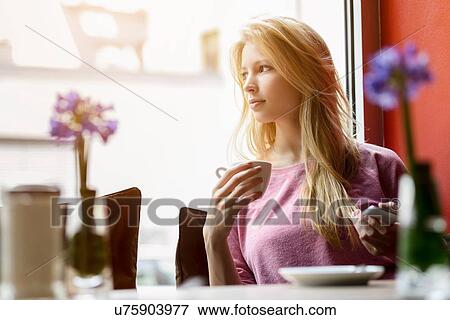 Stock Photo - Young woman gazing out of cafe window whilst drinking coffee. Fotosearch