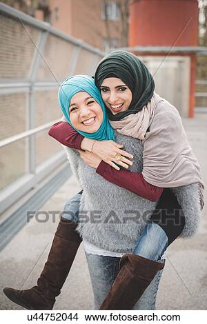 Young woman giving piggyback to friend View Large Photo Image Picture - Young woman giving piggyback to friend. Fotosearch