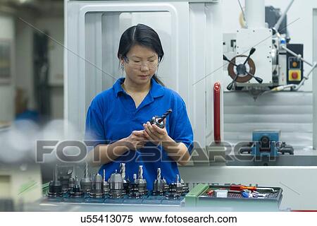 Stock Photography - Young woman holding metal components in industrial workshop. Fotosearch