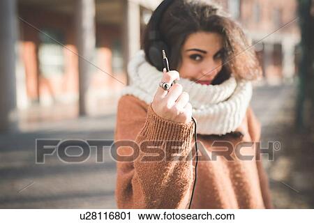 Stock Image - Young woman holding up headphone cable on street. Fotosearch